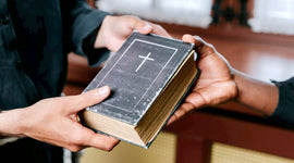 Two people holding a Bible with a cross on the cover in a church setting.