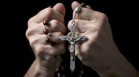 Hands holding a Rosary with crucifix on a black background
