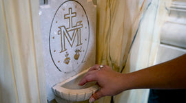 Hand reaching out to dip in a holy water fountain with the Miraculous Medal logo on it