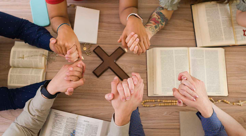 People holding hands an praying next to an olive wood cross