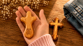 Olive wood comfort cross held in a hand beside a handcrafted cross, showing size and smooth finish from the Holy Land.