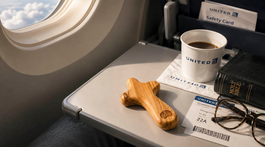 Comfort cross on an airplane table near a window with coffee, bible and glasses next to it.