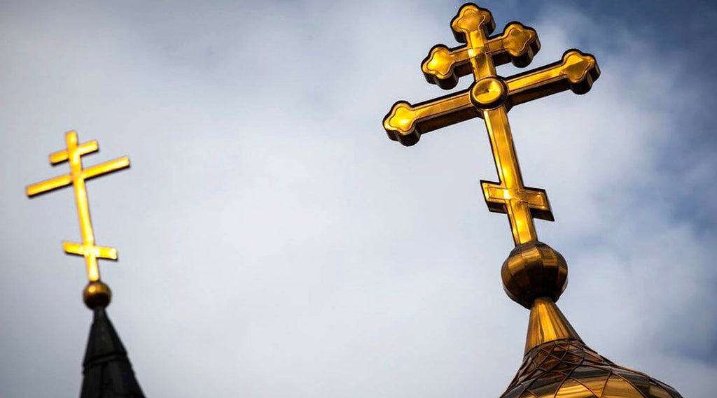 Golden Orthodox crosses atop church domes silhouetted against a cloudy sky, symbolizing the Orthodox Christian faith.