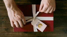 Person tying a ribbon on a gift box with a tag on a wooden surface