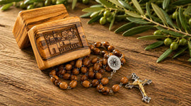 Olive wood rosary and a box with Jerusalem written on it laying on a table next to an olive wood branch