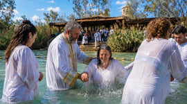 Christian baptism ceremony in the Jordan River as a priest immerses a woman surrounded by fellow believers.