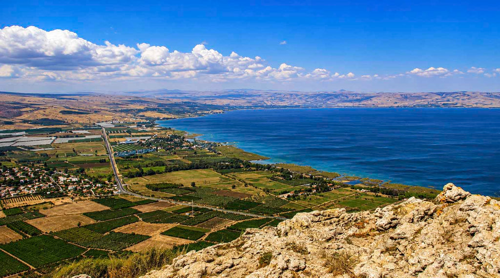 Panoramic view of the Sea of Galilee from Mount Arbel overlooking fields, shoreline, and the Golan Heights.