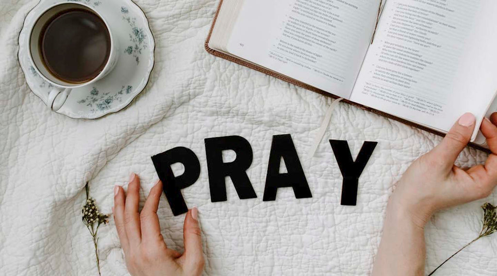 Open book, cup of coffee, and hands with 'PRAY' letters on a textured surface