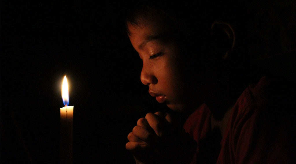 Child praying in dark in front of the candle