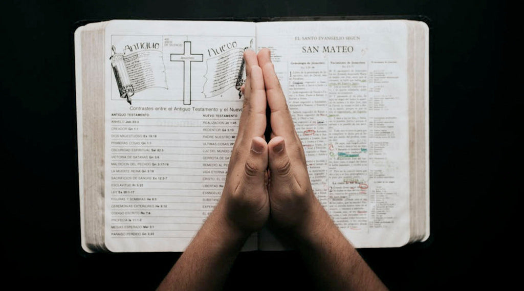 Open Bible with hands clasped on a black background