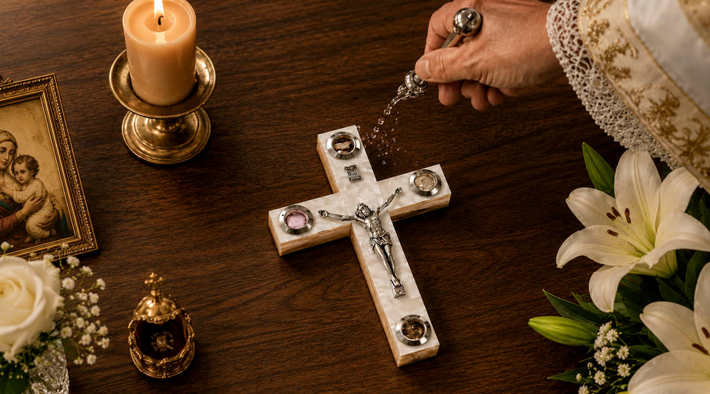 Priest's hand blessing a white cross with holy water and a candle next to it