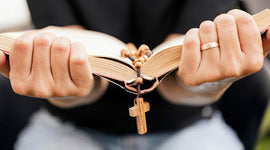Man holding an open bible with a cross rosary, wearing a ring.