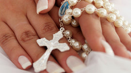 Hands holding a white pearl rosary with Miraculous Medal and silver crucifix during prayer or quiet reflection.