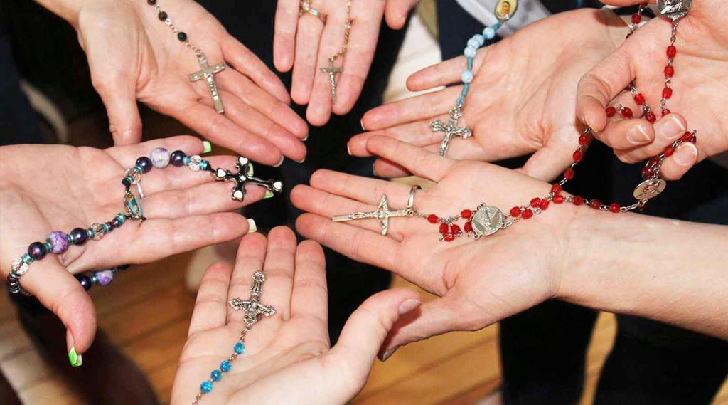 Hands holding rosaries with various types of crosses and beads.