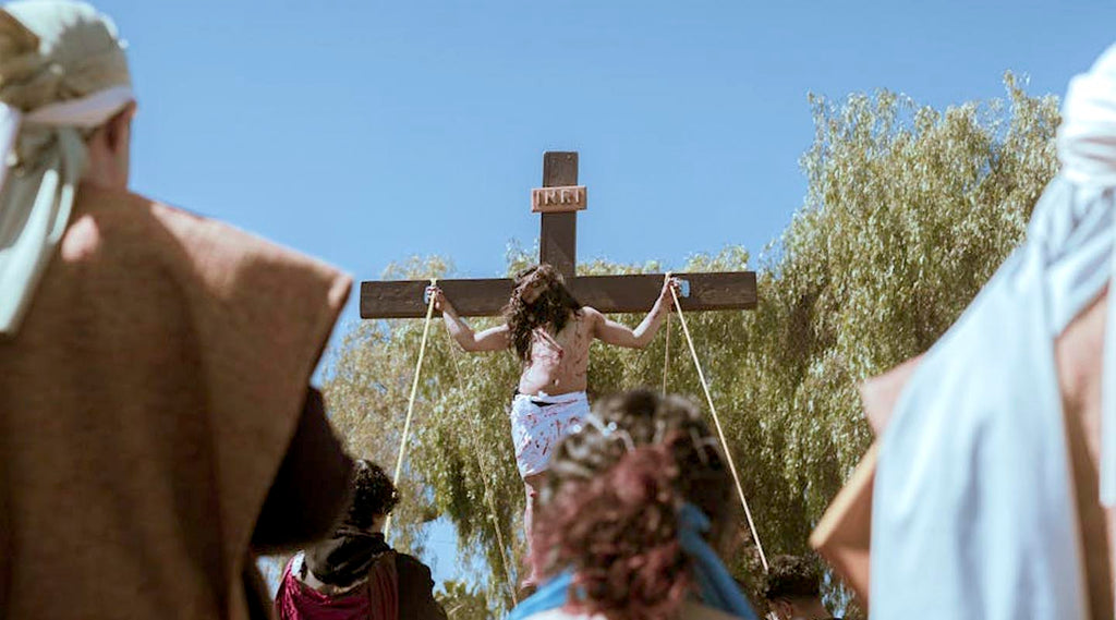 Jesus on a cross with people around, set against a clear blue sky.
