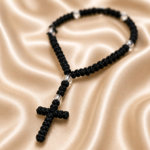 A black knotted prayer rope with a cross and small acrylic spacer beads, on a cream satin fabric.