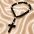 A black knotted prayer rope with a cross and small acrylic spacer beads, on a cream satin fabric.