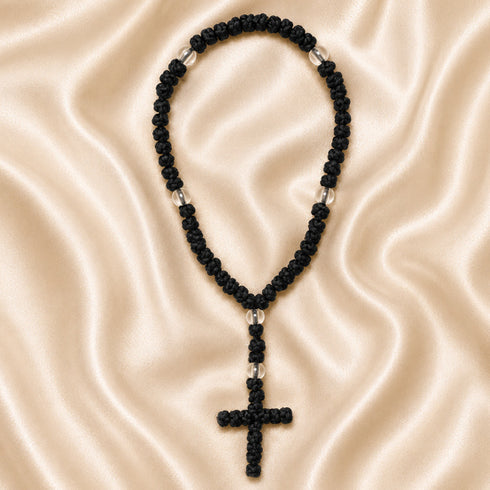 A black knotted cord chotki with a cross and small acrylic spacer beads, on a cream satin fabric.
