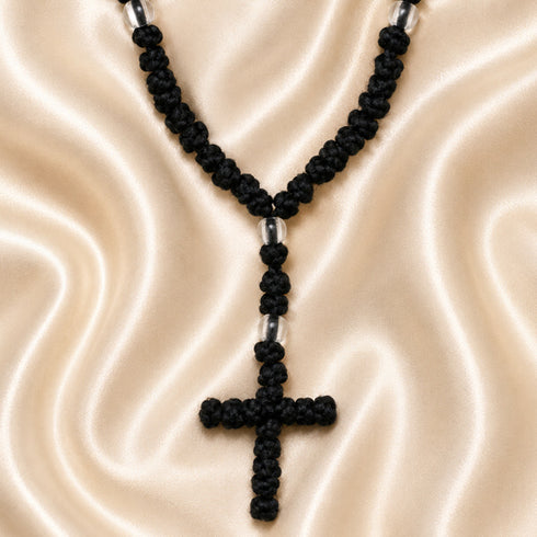 A black knotted cord chotki with a cross and small acrylic spacer beads, on a cream satin fabric.
