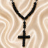 A black knotted cord chotki with a cross and small acrylic spacer beads, on a cream satin fabric.