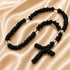 A black knotted cord prayer rope with a cross and clear faceted beads, arranged on a beige satin fabric.