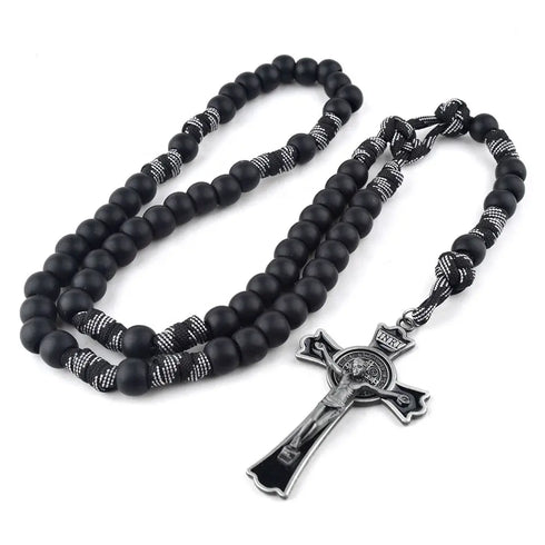 Handcrafted black paracord rosary with 12mm matte beads and St.Benedict cross, laid on white surface.