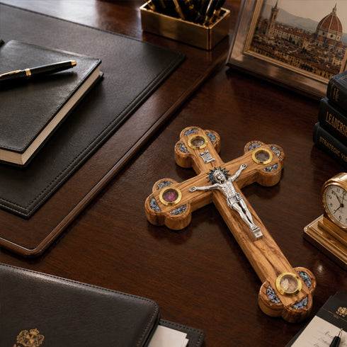 Wooden cross with intricate designs on a wooden desk with books and a clock.