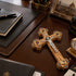 Wooden cross with intricate designs on a wooden desk with books and a clock.