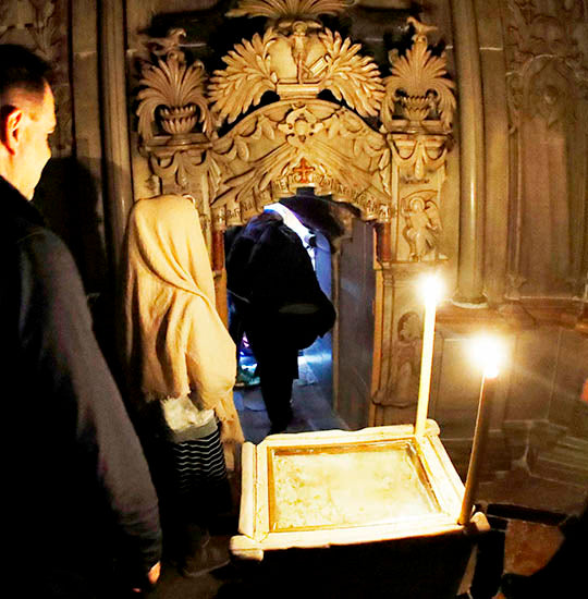 Entrance to the The first chamber of the Aedicula, the Chapel of the Angel with pilgrims and lit by candles.