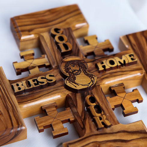 Detail of a handmade olive wood Jerusalem Cross with "God Bless Our Home" and Jesus Christ face engravings, displayed on a white background.