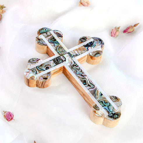 A decorative budded handmade olive wood cross with mother of pearl inlays, placed on a white surface with scattered flower petals around it.