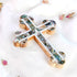 A decorative budded handmade olive wood cross with mother of pearl inlays, placed on a white surface with scattered flower petals around it.