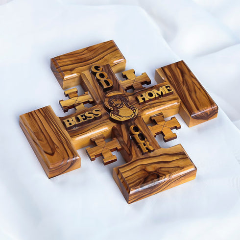 Jerusalem Cross carved from olive wood, featuring engraved blessings and Jesus Christ's face, resting on a white surface.