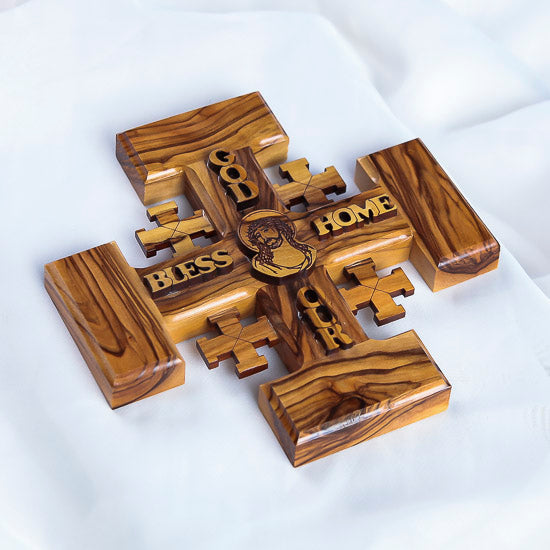 Jerusalem Cross carved from olive wood, featuring engraved blessings and Jesus Christ's face, resting on a white surface.