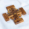 Jerusalem Cross carved from olive wood, featuring engraved blessings and Jesus Christ's face, resting on a white surface.