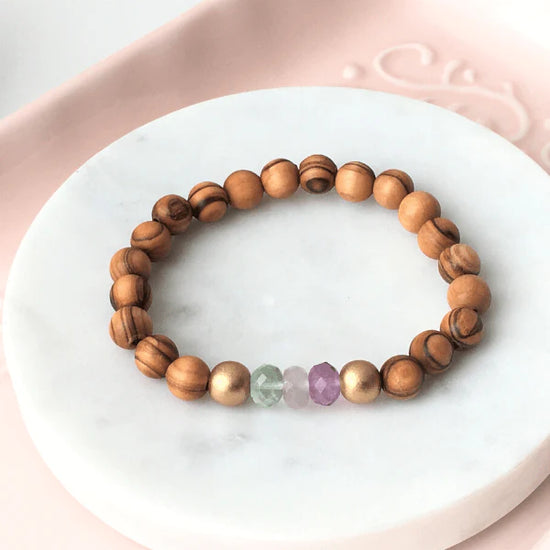 Olive wood bracelet with colourful crystals laid on a white stone and peach colour cloth.