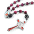 Handmade rosary with red Tiger Eye beads, a Child Jesus centrepiece and a red St. Benedict crucifix, laid on white surface.