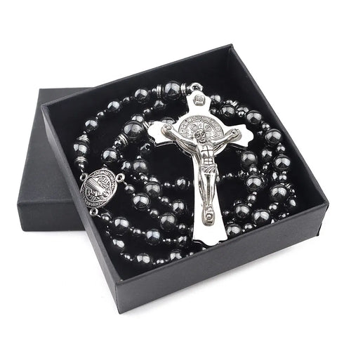 Saint Benedict rosary with dark hematite beads and silver crucifix in a black box, laid on white surface.