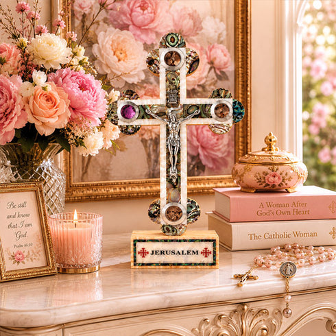 Decorative cross with Jerusalem inscription on a table with flowers and books.