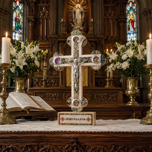 Decorative cross on an altar with candles, flowers, and stained glass windows in the background.
