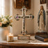 Decorative cross with Jerusalem inscription, candle, statue of a religious figure, and books on a table.