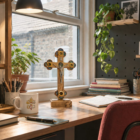 Olive wood Apostles crucifix on a bright home office wall above a desk with everyday work items