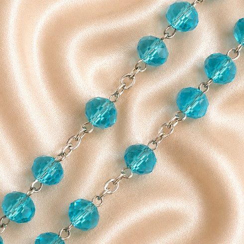 A close-up of a beaded chain necklace with faceted turquoise blue beads connected by silver-toned links.
