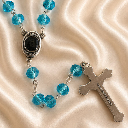 A rosary with turquoise blue beads, a black oval centerpiece engraved with 'TERRA JERUSALEM', and a silver-tone cross pendant.