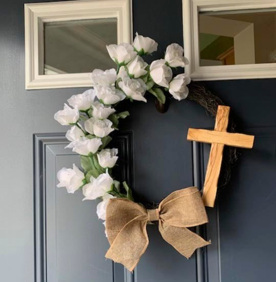 Olive wood thorn cross on a blue entrance door with small windows and flowers.