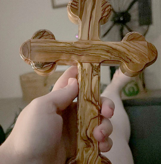 Orthodox budded olive wood cross hand held in a living room background