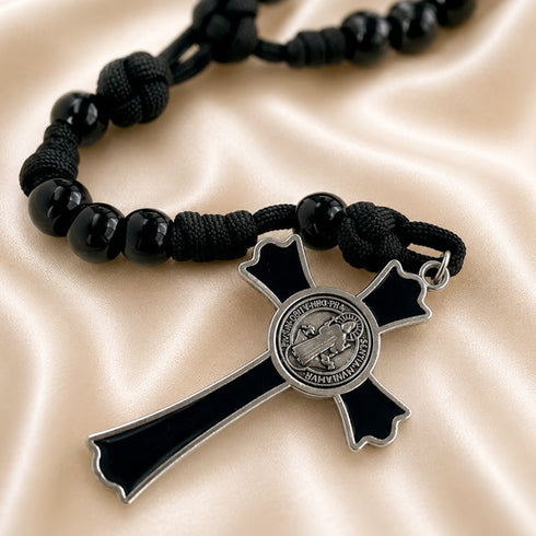 A black cord rosary with black beads and a black-and-silver cross, displayed on a beige satin background.