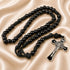 A black beaded rosary with a silver and black crucifix, on a beige satin fabric background.