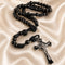 Black rosary knotted centerpiece and a silver-toned crucifix pendant, displayed on champagne satin fabric.
