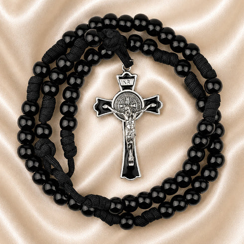 Black beaded rosary with a silver crucifix, on a beige satin fabric background.